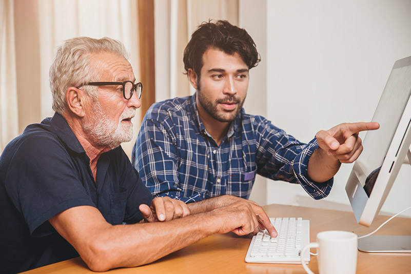 Young man helping older man with computer